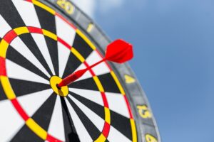 A red dart hits the bullseye on a black, white, and yellow dartboard under a blue sky, symbolizing the precision and effectiveness achieved with the benefits of using paid ads.